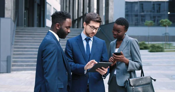 Portret van een vertrekkende jonge man die zijn collega 's informatie op tablet laat zien. Ze staan op straat te kletsen. Conferentie concept — Stockfoto