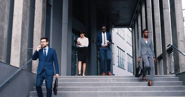 Lleno de alegría. Retrato de larga duración de los socios de negocios ocupados elegantes felices están caminando a lo largo de las escaleras mientras se sienten satisfechos después del trabajo. Concepto gente de negocios — Foto de Stock