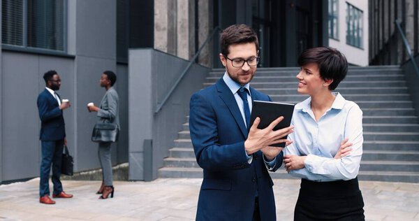 Уверенное дело. Талия портрет молодого серьезного бизнесмена стоит с планшетом рядом со своей милой коллегой-женщиной, пристально глядя на экран. Концепция бизнеса