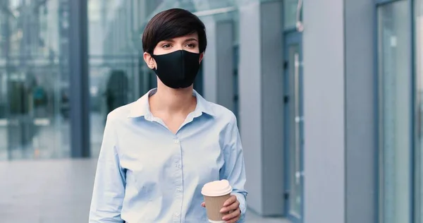 Porträtt av strålande ung affärskvinna bär skyddande mask gå genom gatan och dricka kaffe. Människan och karriären — Stockfoto