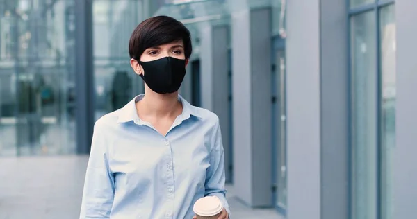 Porträtt av strålande ung affärskvinna bär skyddande mask gå genom gatan och dricka kaffe. Människan och karriären — Stockfoto