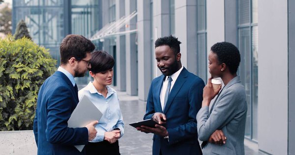 Группа сотрудников, стоящих на улице возле офисного центра. Босс стоит и показывает основные документы на планшете участникам встречи. Концепция бизнеса