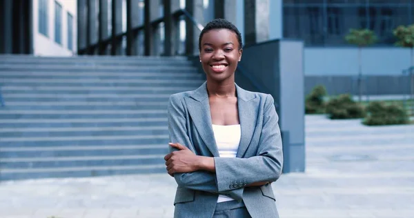 Cintura para cima vista retrato de senhora multirracial sorridente vestindo blusa branca e terno enquanto está perto do centro de negócios e sorrindo. Ela sente-se confiante. — Fotografia de Stock