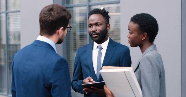 Концепция бизнес-соглашений. Талия портрет очаровательной многорасовой леди, держащейся за руки и подписывающей документы, стоя на улице со своими партнерами