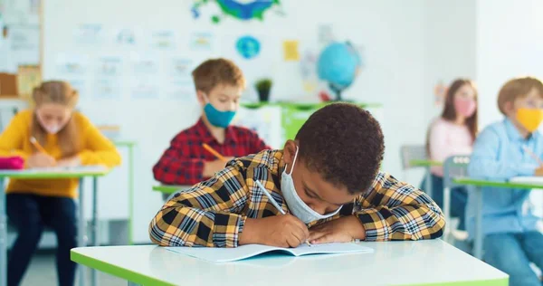 Afro-americano pequeño niño lindo alumno que estudia en la escuela lección sentado en el escritorio de la escuela. Niños caucásicos aprendiendo en el aula Educación de cuarentena covid. Escuela primaria Primer plano concepto de retrato —  Fotos de Stock