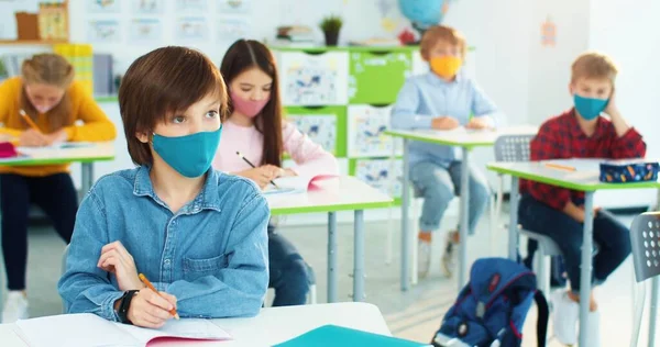 Las maestras dan la mano en el aula midiendo la temperatura del estudiante de primaria caucásica con máscara sentada en el aula en la lección usando termómetro infrarrojo durante el covidio-19. Primer plano retrato —  Fotos de Stock