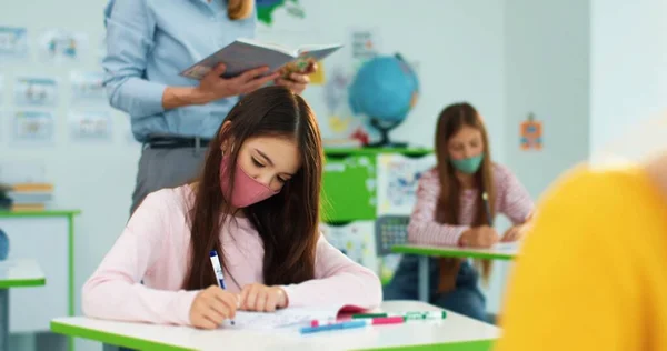 Primer plano retrato de colegiala caucásica haciendo trabajo de clase escribiendo en copybook. Alumnos niños que estudian en la escuela primaria. Educación post-cuarentena. Aprendizaje después de la pandemia de covid-19 en la escuela —  Fotos de Stock