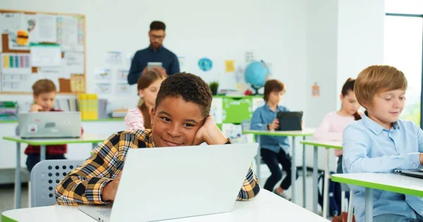 在课堂上用笔记本电脑近距离拍摄快乐的非洲裔美国男孩的肖像。男教师解释背景上使用平板电脑。互联网技术。计算机科学课。现代教育 — 图库照片