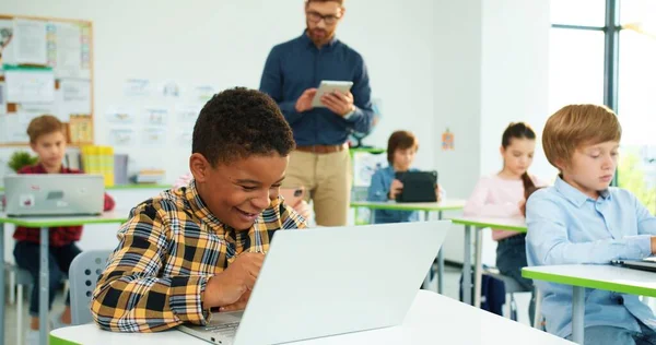 Zamknij się portret szczęśliwy Afroamerykanin nastolatek chłopiec junior stukanie na laptopie podczas lekcji podglądania podczas egzaminu. Mężczyzna nauczyciel za pomocą tabletu na tle technologii internetowej. Klasa informatyki — Zdjęcie stockowe