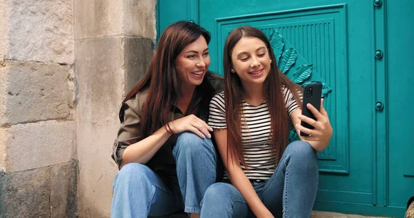 Ας βγάλουμε μια σέλφι. Περιμένετε μέχρι το πορτρέτο άποψη του έφηβος κορίτσι κάνει selfie στο smartphone της με μελαχρινή μητέρα της, ενώ κάθεται στις σκάλες και gesturing. Οικογενειακή έννοια — Φωτογραφία Αρχείου