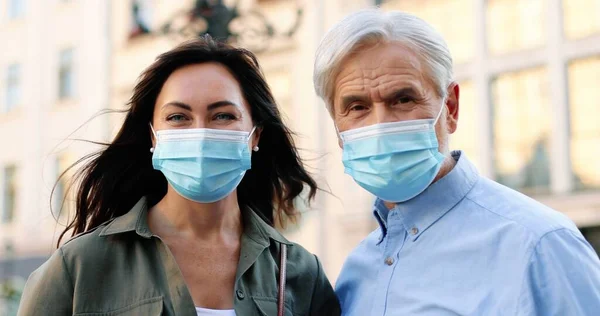 Hija de los padres. Vista del retrato de la morena feliz y su padre con máscaras protectoras mirándose el uno al otro y a la cámara mientras caminan por la ciudad durante la pandemia — Foto de Stock