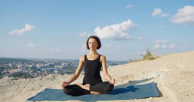 Spor giysileri içinde, meditasyon yapan ve Lotus 'un üzerinde oturan sakin bir kadın manzarası. Yoga ve sağlık konsepti