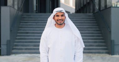 Kandura giyen Arap adam kameraya bakıyor ve BAE 'nin bulanık arka planıyla sokakta dikilirken gülümsüyor. İş konsepti