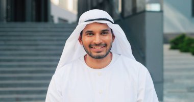 Ulusal giysiler içinde gülümseyen yakışıklı bir işadamının portre görüntüsü. Sokakta büyük ofis binasının yanında duruyor ve kameraya gülümsüyor.