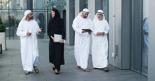 Wandelende Arabieren met kandura op zakenlocatie. Arabische zakenmensen die door de straten van de stad lopen en schotelpasja dragen. Arabisch Midden-Oosten glimlachend tijdens het wandelen en chatten — Stockfoto