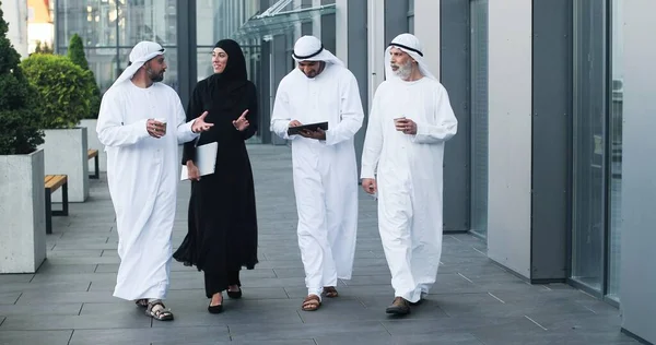 Wandelende Arabieren met kandura op zakenlocatie. Arabische zakenmensen die door de straten van de stad lopen en schotelpasja dragen. Arabisch Midden-Oosten glimlachend tijdens het wandelen en chatten — Stockfoto