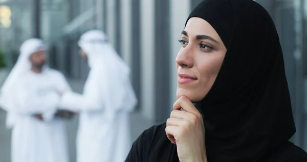 Vista stupenda. Ritratto veduta della donna araba consapevole che indossa un foulard alla testa distogliendo lo sguardo e sorridendo con piacere mentre medita sulla strada vicino al suo ufficio — Foto Stock