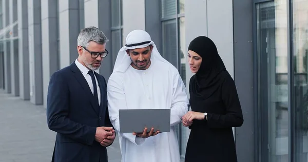 Gemengd business team in Dubai. Zakelijke ontmoeting met mannen met kandura en westerse mensen op straat. Man en vrouw die een hoofddoek dragen en vijf aan elkaar geven — Stockfoto