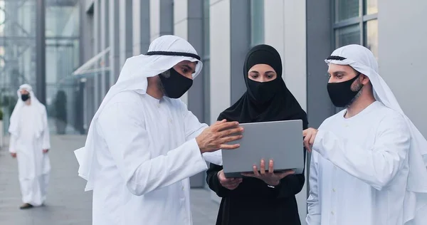 Підніміть портрет мусульманських бізнесменів, які носять захисні маски, обговорюючи щось емоційно, дивлячись на ноутбук. Робота під час пандемії — стокове фото