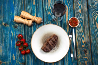 Beyaz tabakta biftek ve masanın üstünde bir bardak şarap.