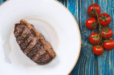 Kızarmış biftek, kiraz domatesleri, mavi ahşap masada tuz ve biber..