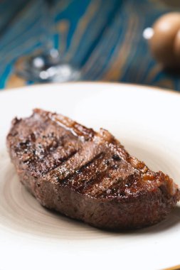 Taze ızgara et. Mavi ahşap arka planda beyaz tabakta baharatlı biftekler.