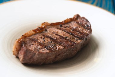 Taze ızgara et. Mavi ahşap arka planda beyaz tabakta baharatlı biftekler.