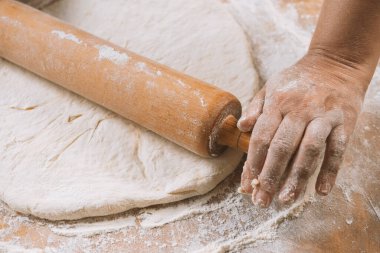 Şef masada merdaneyle hamuru yuvarlıyor. Eller yakın plan. Makarna, ekmek, spagetti, khachapuri, yemek konsepti.
