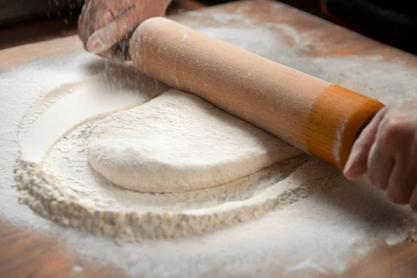 Baker kneading dough for pizza preparation. Chef cook making dough for baking pie on wooden table. Process preparation homemade pastry. Cooking pasta, bread,spaghetti,khachapuri, food concept