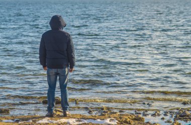 Yalnız bir adam boş bir deniz sahilinde dikiliyor ve soğuk bulutlu bir sonbahar gününde uzaklığa bakıyor, arkadan bakıyor..