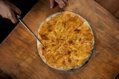 Ahşap arka planda ev yapımı etli turta kesen kişi. Bulgar banitsa, Gürcü khachapuri, Yunan tiropita