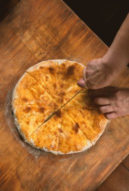 Ahşap arka planda ev yapımı peynirli turta kesen biri. Bulgar banitsa, Gürcü khachapuri, Yunan tiropita