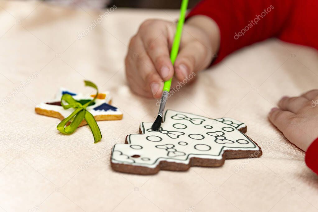 Little boy draws food paints on Christmas homemade gingerbread cookies . Christmas concept .