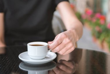 Bir kız kafede kahve içiyor. Kahve dükkanının arka planında, ahşap sehpanın üzerinde beyaz kahve fincanı.