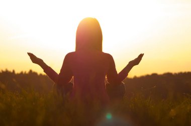 Gün batımında yoga yapan bir kadının arka ışığı.
