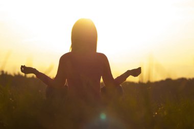 Gün batımında yoga yapan bir kadının arka ışığı.