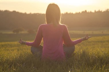 Gün batımında yoga yapan bir kadının arka ışığı.