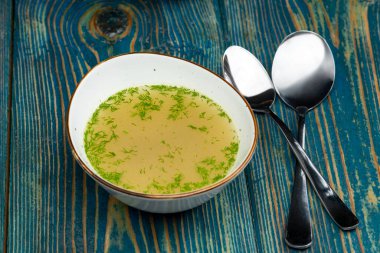 Mavi masadaki beyaz kasede tavuk suyu çorbası.