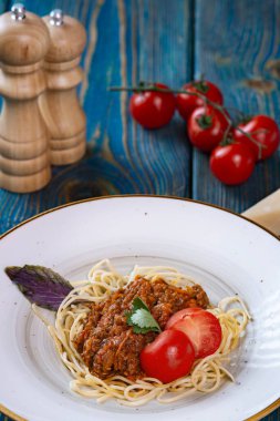 Etli makarna, domates sosu ve mavi ahşap masada sebzeler.