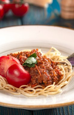 Beyaz tabakta spagetti bolonez makarna, tuz, biber, peynir ve domates mavi ahşap arka planda..