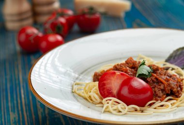 Beyaz tabakta spagetti bolonez makarna, tuz, biber, peynir ve domates mavi ahşap arka planda..