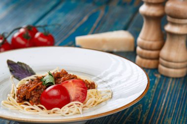 Etli makarna, domates sosu ve mavi ahşap masada sebzeler.