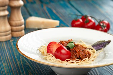 Etli makarna, domates sosu ve mavi ahşap masada sebzeler.