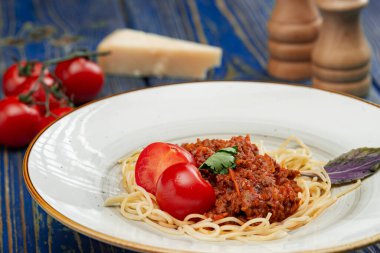 Kıymalı spagetti ve mavi ahşap arka planda vişneli domates..