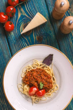 Beyaz tabakta spagetti bolonez makarna, tuz, biber, peynir ve domatesler mavi ahşap arka planda.
