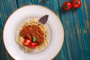 Mavi ahşap arka planda kıyma ve kiraz domatesli lezzetli spagetti. Üst manzara, düz uzanma