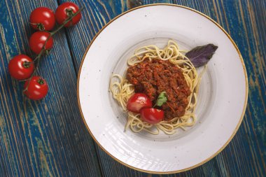 Beyaz tabakta spagetti bolonez makarna, tuz, biber, peynir ve domatesler mavi ahşap arka planda.