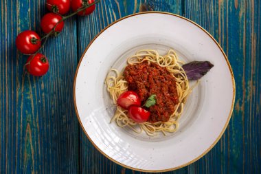 Beyaz tabakta spagetti bolonez makarna, tuz, biber, peynir ve domatesler mavi ahşap arka planda.