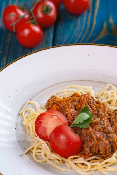 Beyaz tabakta spagetti bolonez makarna, tuz, biber, peynir ve domates mavi ahşap arka planda..