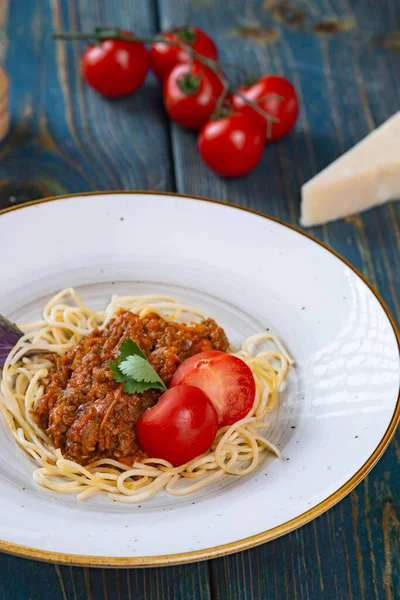 Etli makarna, domates sosu ve mavi ahşap masada sebzeler.
